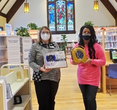 Two people at Kentville Regional Library holding the donated AED and its presentation certificate.